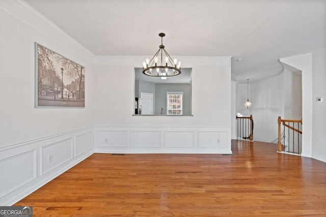 spare room featuring wood-type flooring, ornamental molding, and an inviting chandelier