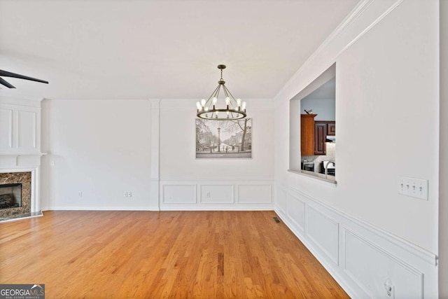 unfurnished dining area featuring a fireplace, ceiling fan with notable chandelier, crown molding, and light hardwood / wood-style floors