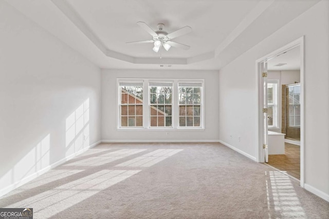 carpeted empty room featuring ceiling fan and a raised ceiling