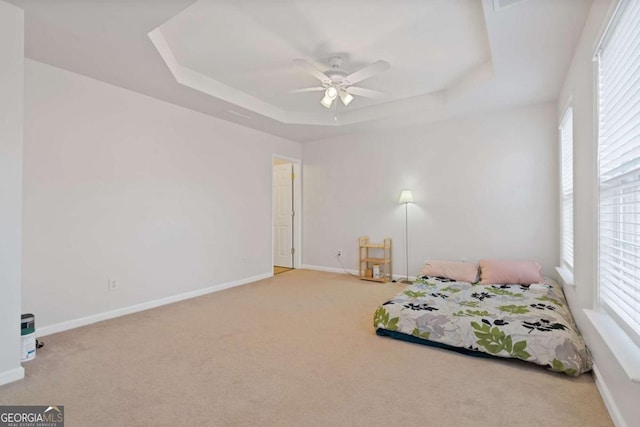 unfurnished bedroom with light carpet, ceiling fan, a tray ceiling, and multiple windows