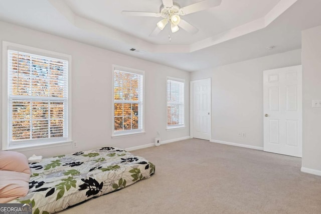 carpeted bedroom with ceiling fan and a tray ceiling