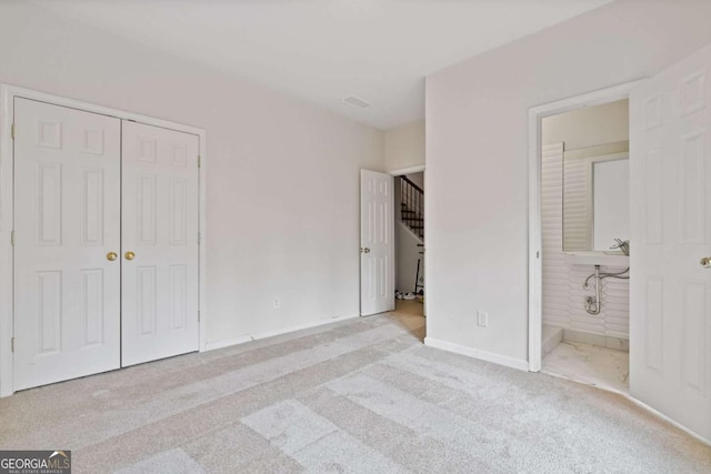 unfurnished bedroom featuring light carpet, a closet, and ensuite bath