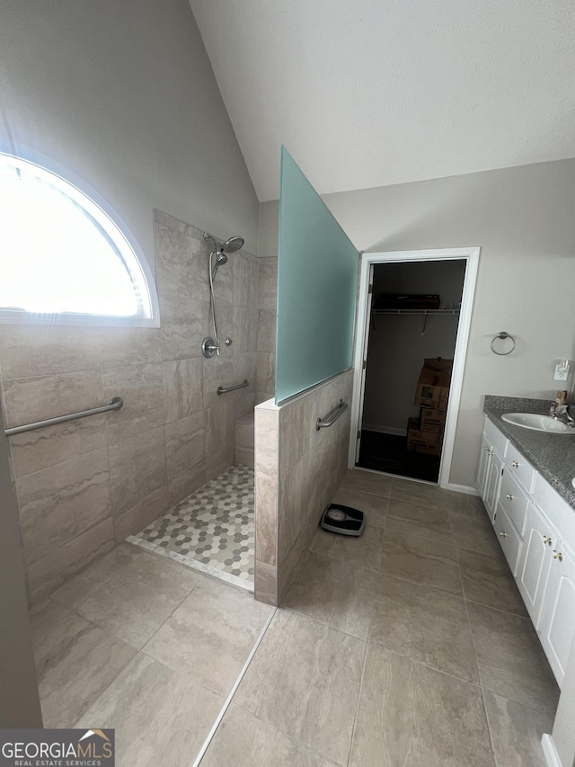 bathroom with vaulted ceiling, a tile shower, tile patterned floors, and vanity