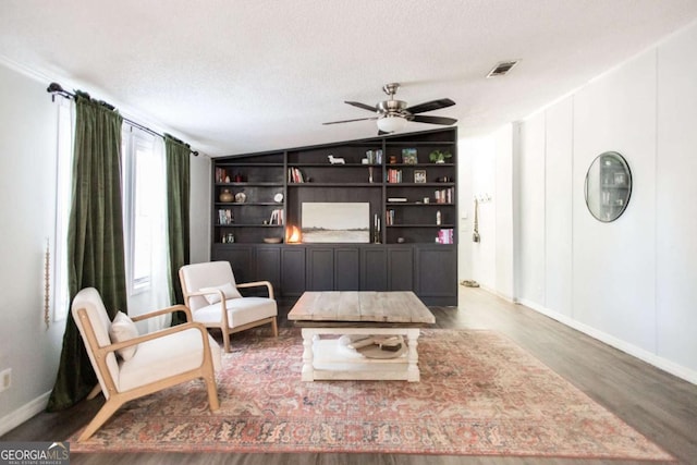 sitting room with hardwood / wood-style floors, ceiling fan, a textured ceiling, built in features, and vaulted ceiling