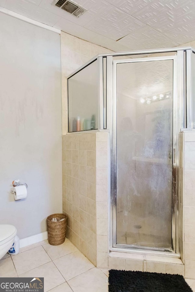 bathroom with toilet, a shower with door, and tile patterned flooring