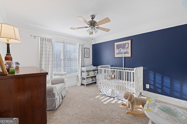 bedroom with ceiling fan, a nursery area, crown molding, and carpet flooring