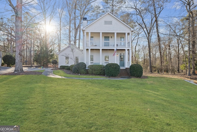 neoclassical home featuring a balcony, covered porch, and a front yard