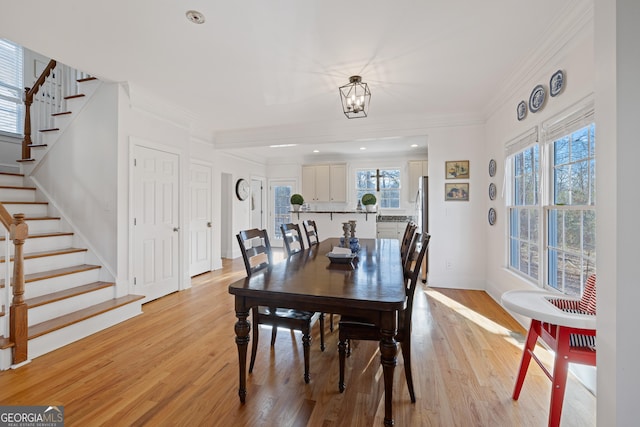 dining space with light hardwood / wood-style flooring, ornamental molding, and a notable chandelier