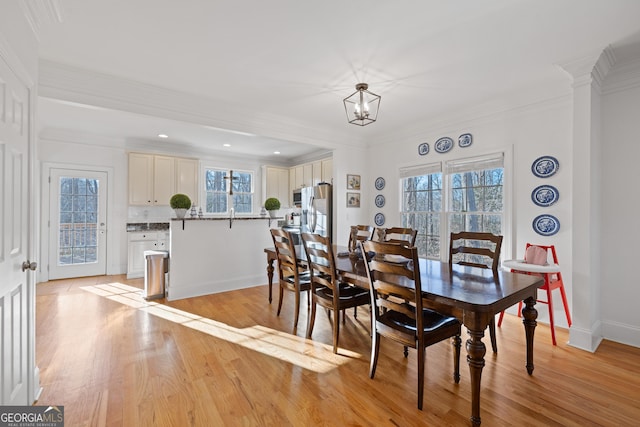 dining area featuring light wood-type flooring, a wealth of natural light, crown molding, and a notable chandelier