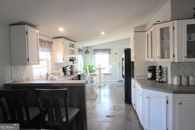 kitchen featuring lofted ceiling, black fridge, decorative backsplash, white cabinetry, and stainless steel range with electric stovetop