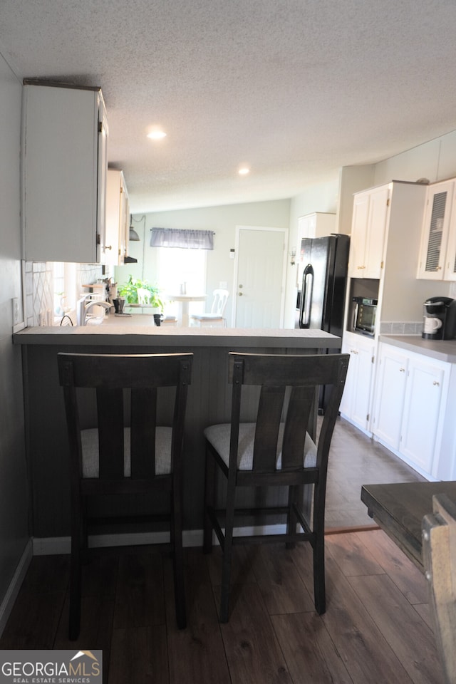 kitchen featuring a breakfast bar area, white cabinets, dark hardwood / wood-style flooring, and a textured ceiling