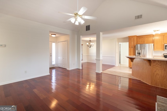 unfurnished living room featuring dark hardwood / wood-style flooring, high vaulted ceiling, ceiling fan with notable chandelier, and decorative columns