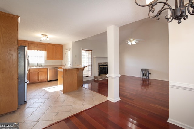 kitchen with vaulted ceiling, a fireplace, a kitchen breakfast bar, stainless steel appliances, and light wood-type flooring