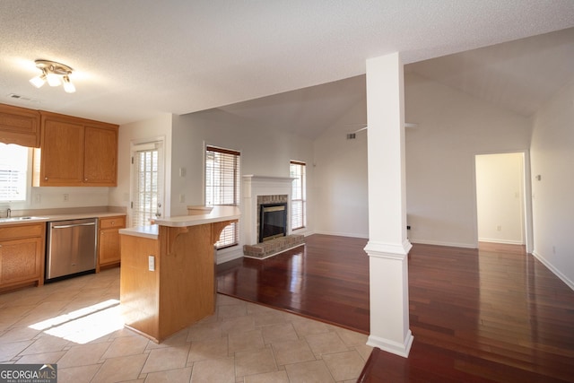 kitchen with a kitchen bar, lofted ceiling, stainless steel dishwasher, a fireplace, and light hardwood / wood-style floors