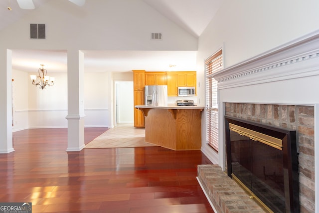 unfurnished living room featuring high vaulted ceiling, dark hardwood / wood-style flooring, ceiling fan, a fireplace, and decorative columns