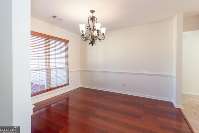 spare room featuring an inviting chandelier and dark wood-type flooring