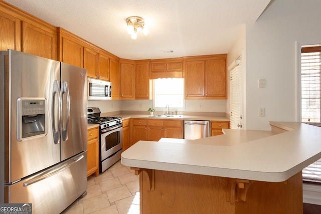 kitchen with light tile patterned flooring, stainless steel appliances, a kitchen bar, and sink