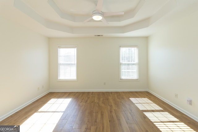 unfurnished room with a raised ceiling, hardwood / wood-style flooring, and ceiling fan