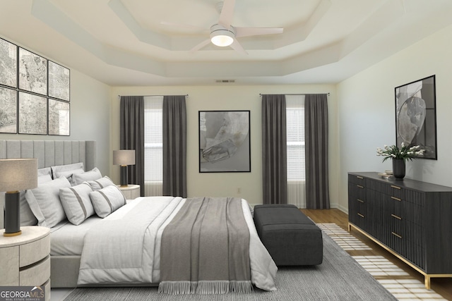 bedroom with ceiling fan, a tray ceiling, and hardwood / wood-style floors