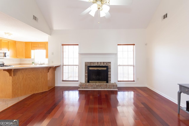 unfurnished living room with ceiling fan, high vaulted ceiling, dark wood-type flooring, and a fireplace