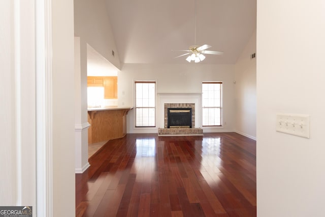 unfurnished living room featuring ceiling fan, dark hardwood / wood-style floors, high vaulted ceiling, and a brick fireplace