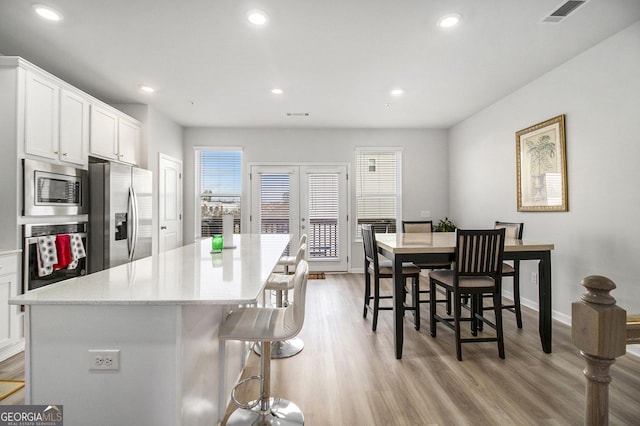 kitchen with white cabinets, appliances with stainless steel finishes, a kitchen island, light wood-type flooring, and a breakfast bar