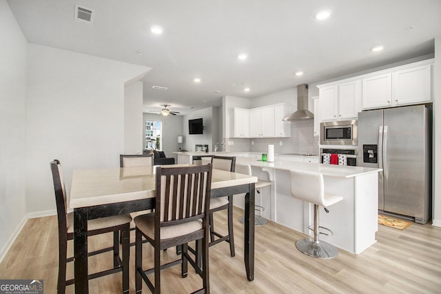 kitchen featuring white cabinetry, wall chimney range hood, stainless steel appliances, tasteful backsplash, and a kitchen breakfast bar