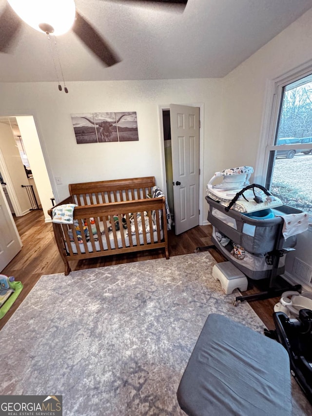 bedroom with ceiling fan, hardwood / wood-style floors, a textured ceiling, and a crib