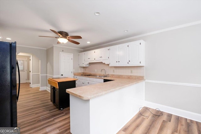 kitchen featuring kitchen peninsula, backsplash, black fridge, white cabinets, and sink