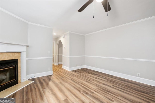 unfurnished living room featuring ceiling fan, a high end fireplace, crown molding, and light wood-type flooring