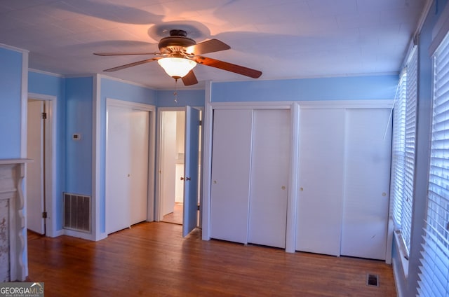 unfurnished bedroom with ceiling fan, wood-type flooring, and multiple closets