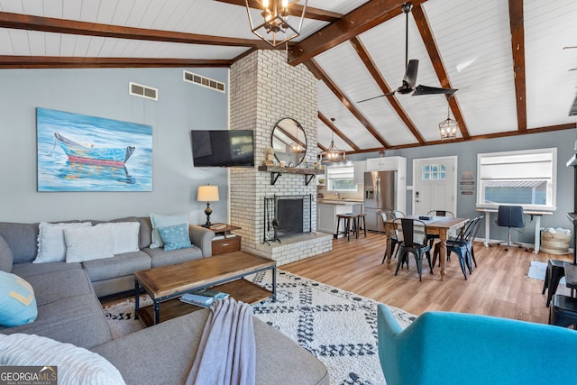 living room with ceiling fan, lofted ceiling with beams, a brick fireplace, and light hardwood / wood-style floors