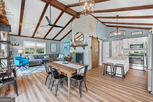 dining room with a barn door, a brick fireplace, light wood-type flooring, high vaulted ceiling, and beam ceiling