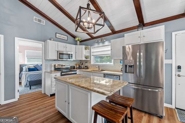 kitchen featuring decorative light fixtures, a center island, beam ceiling, stainless steel appliances, and white cabinets