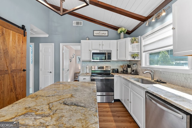 kitchen with white cabinets, appliances with stainless steel finishes, vaulted ceiling with beams, sink, and a barn door