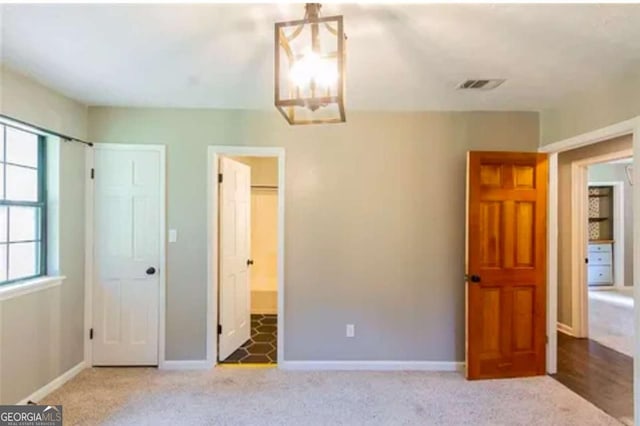 unfurnished bedroom with an inviting chandelier, carpet floors, and ensuite bath