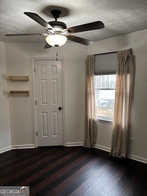 empty room with ceiling fan, dark hardwood / wood-style floors, and a textured ceiling