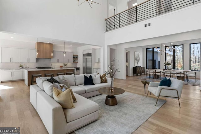 living room with light hardwood / wood-style floors, a chandelier, and a towering ceiling