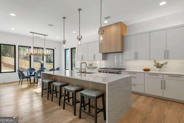 kitchen with decorative light fixtures, white cabinets, a kitchen island with sink, and sink