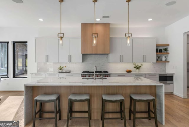 kitchen with decorative light fixtures, white cabinets, and a center island with sink