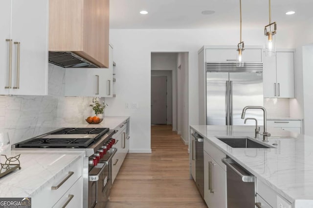 kitchen with hanging light fixtures, white cabinets, premium appliances, and light stone counters