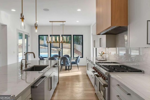 kitchen featuring white cabinetry, appliances with stainless steel finishes, hanging light fixtures, light stone counters, and sink