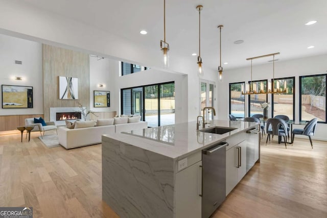 kitchen with pendant lighting, sink, an island with sink, white cabinets, and light stone counters