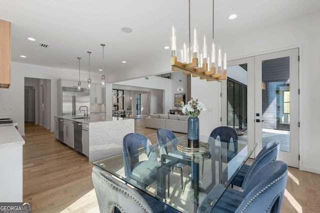 dining room with light wood-type flooring, a notable chandelier, french doors, and sink