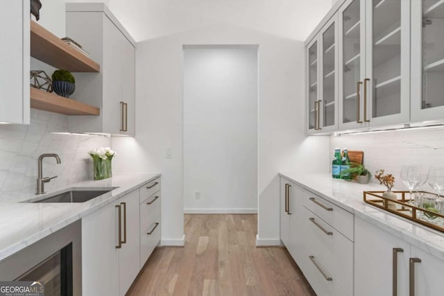 kitchen with white cabinetry, light hardwood / wood-style flooring, light stone counters, and sink