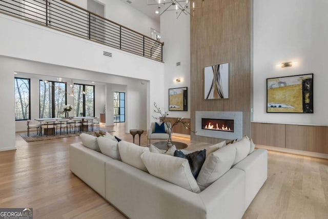 living room featuring light hardwood / wood-style floors, an inviting chandelier, a towering ceiling, and a fireplace