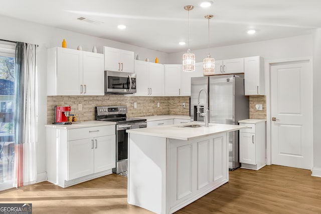 kitchen featuring appliances with stainless steel finishes, white cabinetry, hanging light fixtures, a kitchen island with sink, and light wood-type flooring