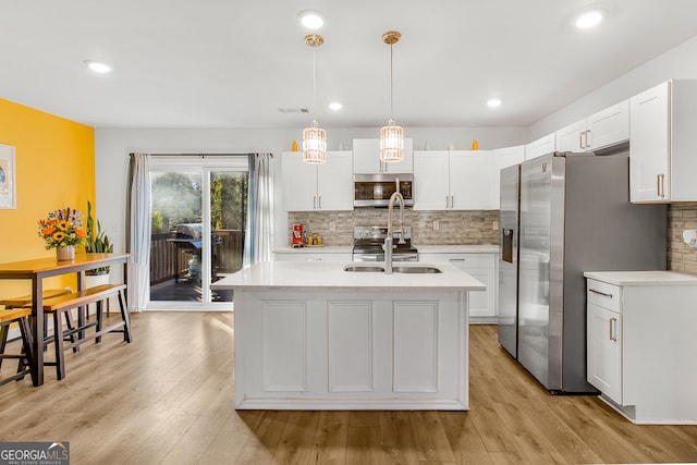 kitchen featuring decorative light fixtures, white cabinetry, a kitchen island with sink, decorative backsplash, and stainless steel appliances