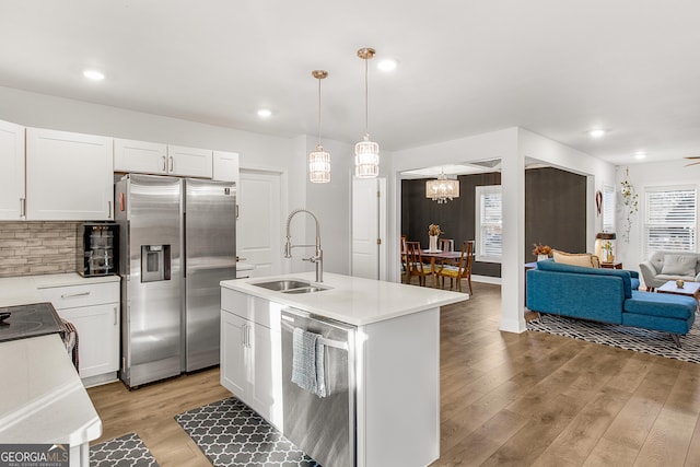 kitchen with appliances with stainless steel finishes, sink, decorative light fixtures, white cabinetry, and a center island with sink