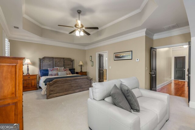 bedroom featuring light carpet, ceiling fan, connected bathroom, a raised ceiling, and crown molding